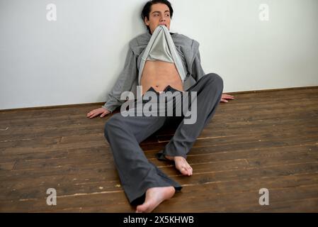 homme fou alcoolique ivre assis sur le sol dans le salon. concept déprimé gaspillé et triste. photo pleine longueur. folie, folie Banque D'Images