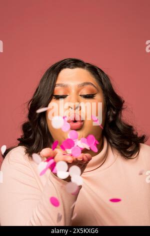 Portrait studio de femme soufflant des confettis Banque D'Images