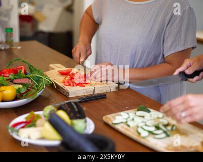 Gros plan des mains des femmes coupant des tomates au comptoir de la cuisine Banque D'Images