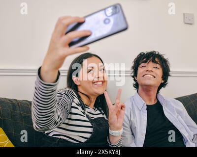 Frère et soeur assis sur le canapé et prenant selfie Banque D'Images