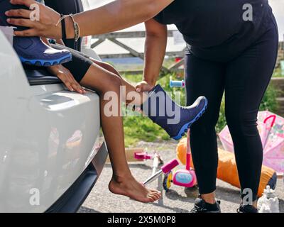 Mère mettant des chaussures en caoutchouc sur sa fille Banque D'Images