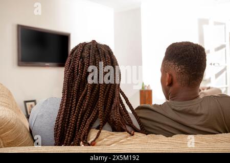 Frères et sœurs assis sur le canapé devant la télévision Banque D'Images