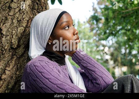 Royaume-Uni, Londres, jeune femme portant le hijab assis près du tronc d'arbre Banque D'Images