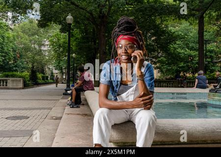 USA, Portrait de jeune femme assise sur le mur dans le parc, parlant sur téléphone intelligent Banque D'Images