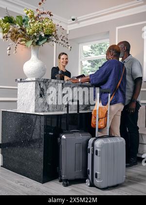 Royaume-Uni, couple d'âge mûr avec valises à la réception de l'hôtel Banque D'Images