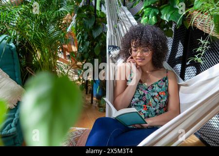 Femme assise dans un hamac et lisant un livre Banque D'Images