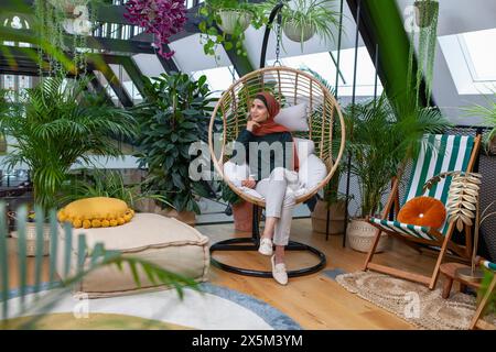 Femme portant le foulard assis dans la chaise balançoire Banque D'Images