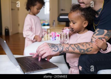 Père travaillant à la maison et prenant soin des filles Banque D'Images