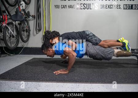 Homme avec une jambe prothétique faisant des pompes dans la salle de gym avec fils sur le dos Banque D'Images