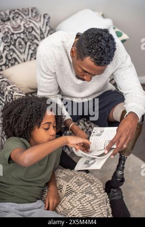 Homme avec un livre de lecture de jambe prothétique avec son fils sur le canapé Banque D'Images