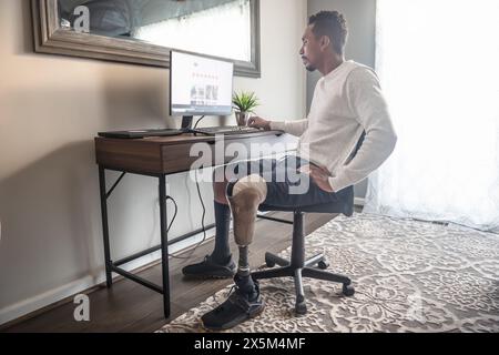 Homme avec prothèse de jambe utilisant l'ordinateur à domicile Banque D'Images