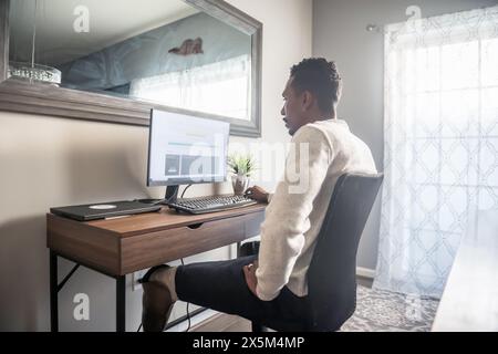 Homme avec prothèse de jambe utilisant l'ordinateur à domicile Banque D'Images