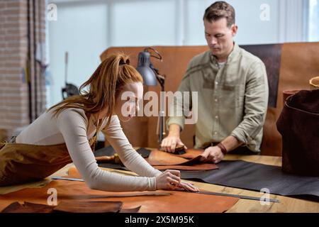 jeune belle femme cordonnier concentré sur fmarking, piercing matériau naturel. gros plan vue latérale shot.guy utilise un pinceau dans l'arrière-plan flou de la photo Banque D'Images