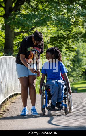 Adolescente (16-17) en fauteuil roulant avec un ami marchant dans le parc Banque D'Images