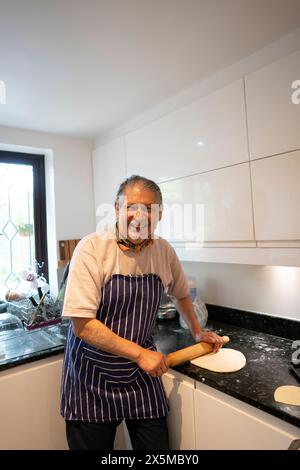 Portrait d'homme senior souriant roulant la pâte à pizza dans la cuisine Banque D'Images