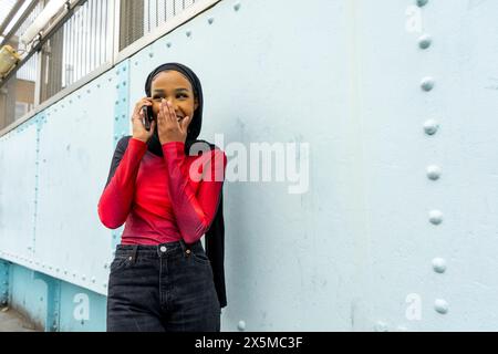 Jeune femme souriante portant le hijab parlant sur un téléphone intelligent Banque D'Images
