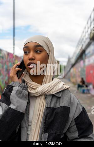 Jeune femme portant le hijab parlant sur téléphone intelligent à l'extérieur Banque D'Images