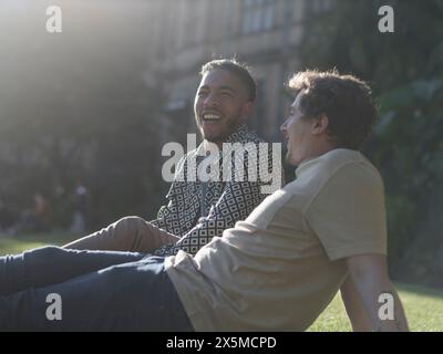 Royaume-Uni, South Yorkshire, couple gay souriant se relaxant sur la pelouse dans le parc Banque D'Images