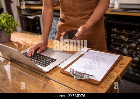 Royaume-Uni, Londres, milieu de section du propriétaire de café utilisant un ordinateur portable et un téléphone intelligent au comptoir Banque D'Images