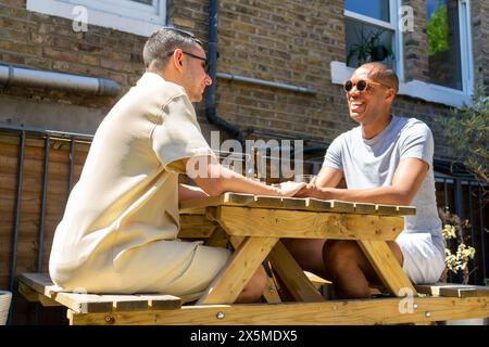 Royaume-Uni, Londres, couple gay souriant se tenant la main à la table de pique-nique Banque D'Images