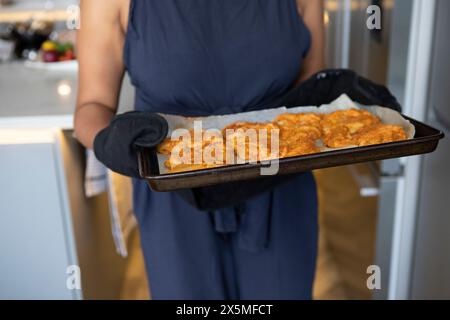 Royaume-Uni, Londres, section médiane de la femme tenant une plaque de cuisson avec de la nourriture dans la cuisine Banque D'Images