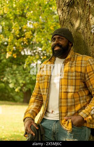 Homme souriant appuyé sur le tronc d'arbre dans le parc en automne Banque D'Images