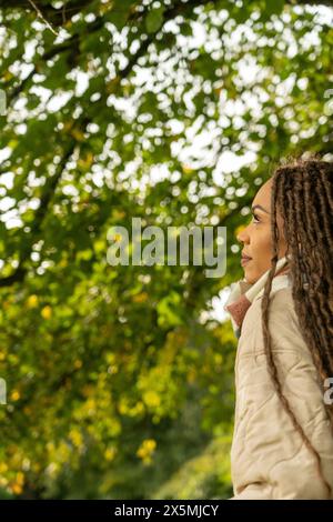 Femme avec des dreadlocks regardant les arbres dans le parc en automne Banque D'Images