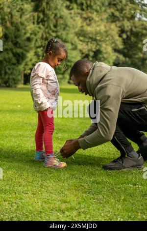 Homme attachant des chaussures de filles dans le parc Banque D'Images