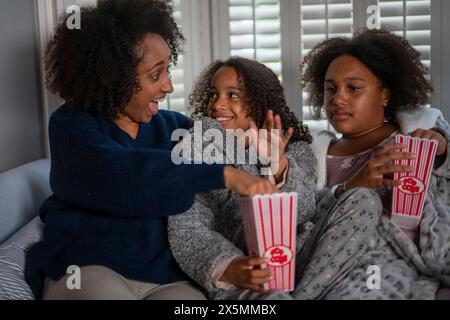 Femme souriante avec des filles appréciant le pop-corn sur le canapé Banque D'Images