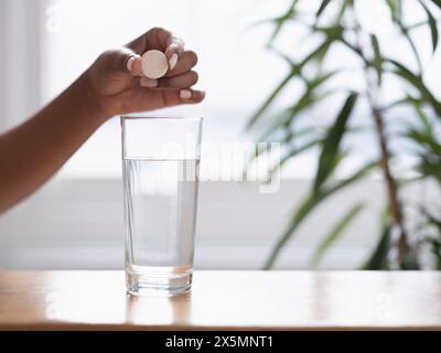 Gros plan de la main des femmes laissant tomber le comprimé effervescent dans un verre d'eau Banque D'Images