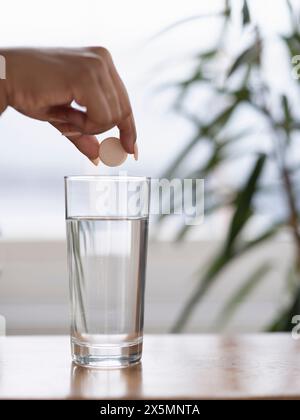 Gros plan de la main des femmes laissant tomber le comprimé effervescent dans un verre d'eau Banque D'Images