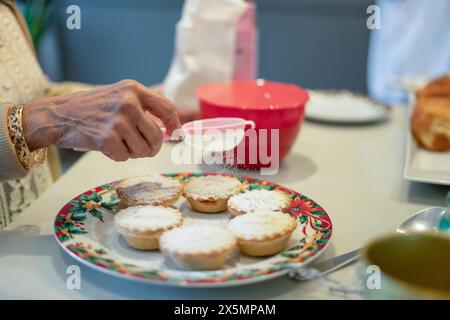 Gros plan d'une femme âgée saupoudrant du sucre en poudre sur des cupcakes Banque D'Images