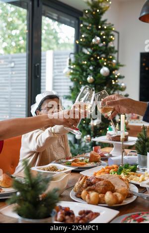 Famille portant des couronnes en papier grillant pendant le dîner de Noël Banque D'Images