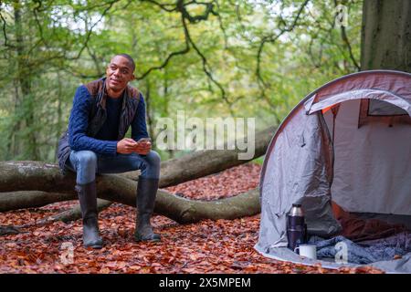 Homme utilisant un téléphone intelligent tout en campant dans la forêt à l'automne Banque D'Images