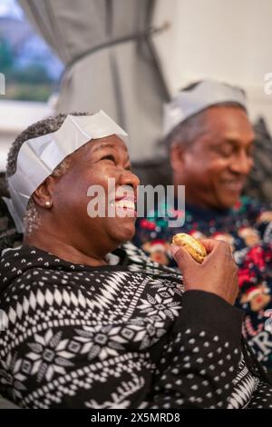 Couple senior assis sur le canapé mangeant des biscuits de Noël Banque D'Images