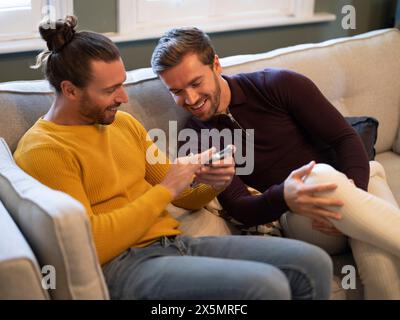 Couple gay regardant le téléphone tout en se relaxant sur le canapé à la maison Banque D'Images