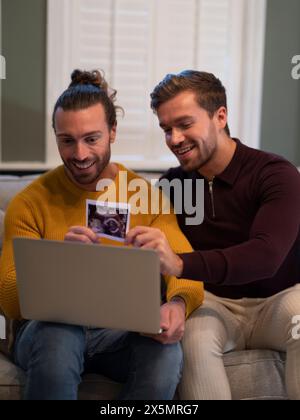 Couple gay montrant l'échographie d'un bébé lors d'un appel vidéo à la maison Banque D'Images