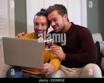 Couple gay montrant l'échographie d'un bébé lors d'un appel vidéo à la maison Banque D'Images
