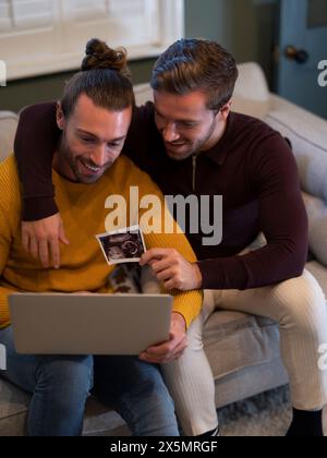 Couple gay montrant l'échographie d'un bébé lors d'un appel vidéo à la maison Banque D'Images