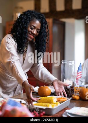 Femme souriante mettant un plat de casserole avec des légumes sur la table de Thanksgiving Banque D'Images