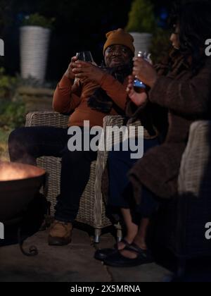 Homme et femme assis près de la fosse de feu sur le patio Banque D'Images