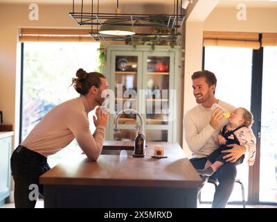 Couple gay nourrissant bébé fille dans la cuisine Banque D'Images