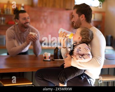 Couple gay nourrissant bébé fille dans la cuisine Banque D'Images