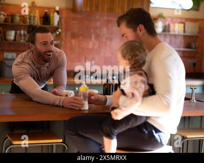 Couple gay nourrissant bébé fille dans la cuisine Banque D'Images