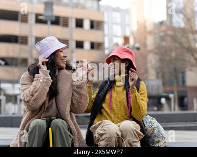 Deux jeunes femmes en milieu urbain, essayant des chapeaux Banque D'Images