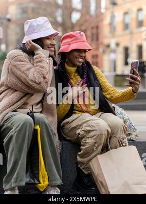 Deux jeunes femmes en milieu urbain, utilisant un smartphone pour prendre des selfies Banque D'Images