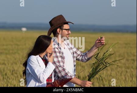 Agriculteur et femme agronmiste en manteau blanc debout dans le champ de blé au début de l'été et vérifiant la croissance des cultures Banque D'Images