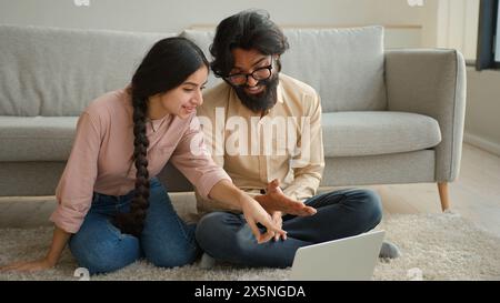 Couple multiracial homme arabe et femme indienne sur le plancher famille couple propriétaires femme petite amie et mari petit ami regardant le film portable Smart TV Banque D'Images