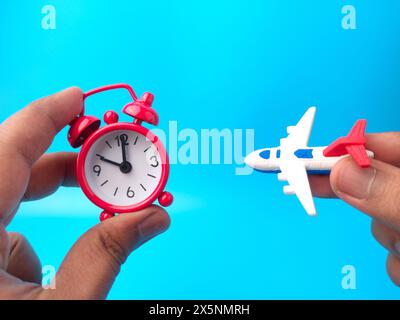 Main tenant l'horloge et les jouets avion sur un fond bleu. Idée de concept de voyage. Banque D'Images