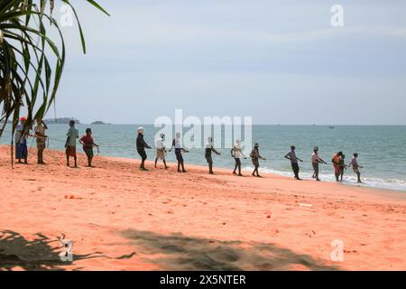 Unawatuna, Sri Lanka 09 février 2023 groupe d'hommes en vêtements d'été de différentes couleurs aidant les pêcheurs à tirer sur un grand filet de pêche de l'océan A. Banque D'Images